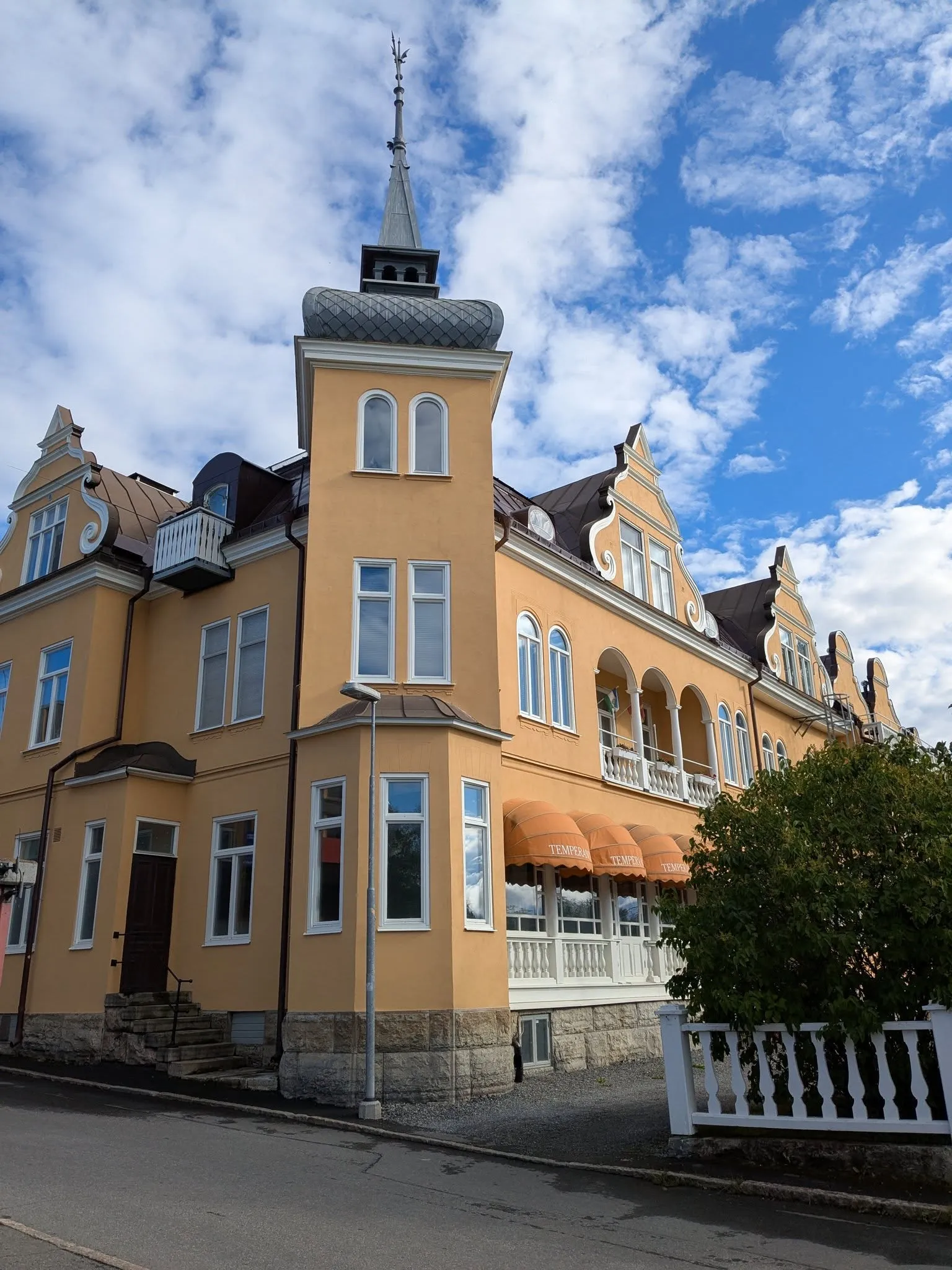 Temperance i sommarljus: gult Jugendhus med torn, svängda gavlar och orange-vita markiser mot blå himmel.